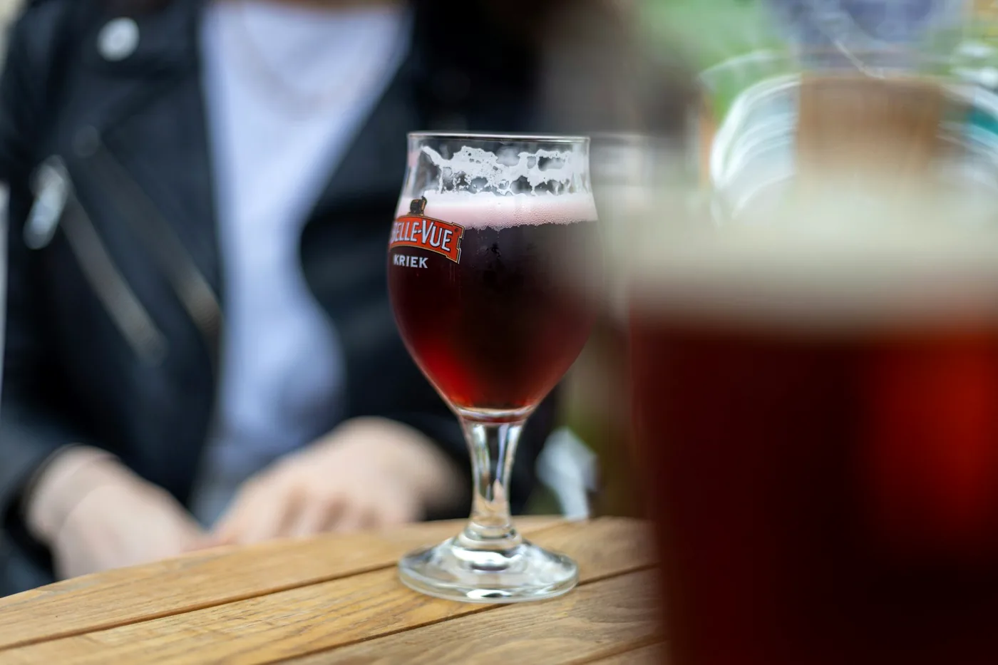 A dark Belgian ale in a stemmed branded chalice on a wooden table