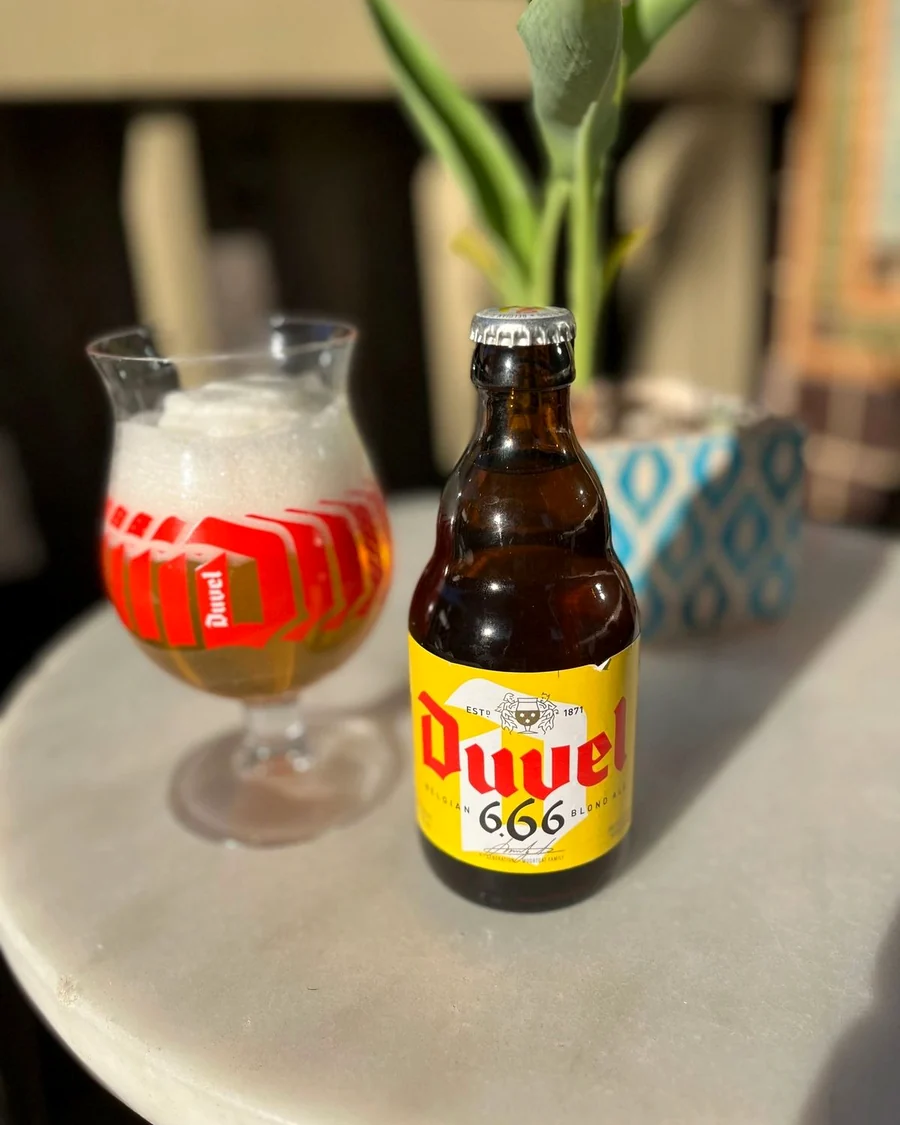 A Duvel bottle beside a tulip glass of pale beer on a marble table