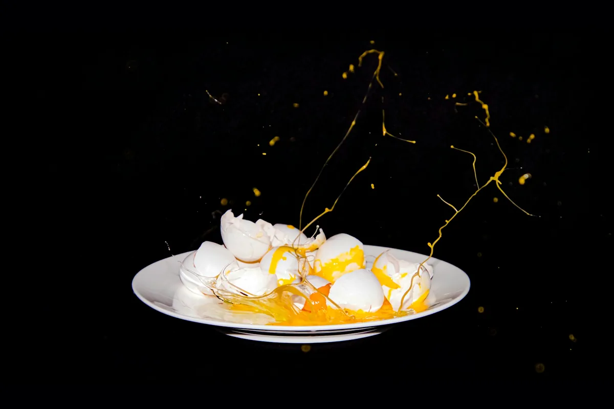 An egg breaking and splashing over a white plate against a dark background