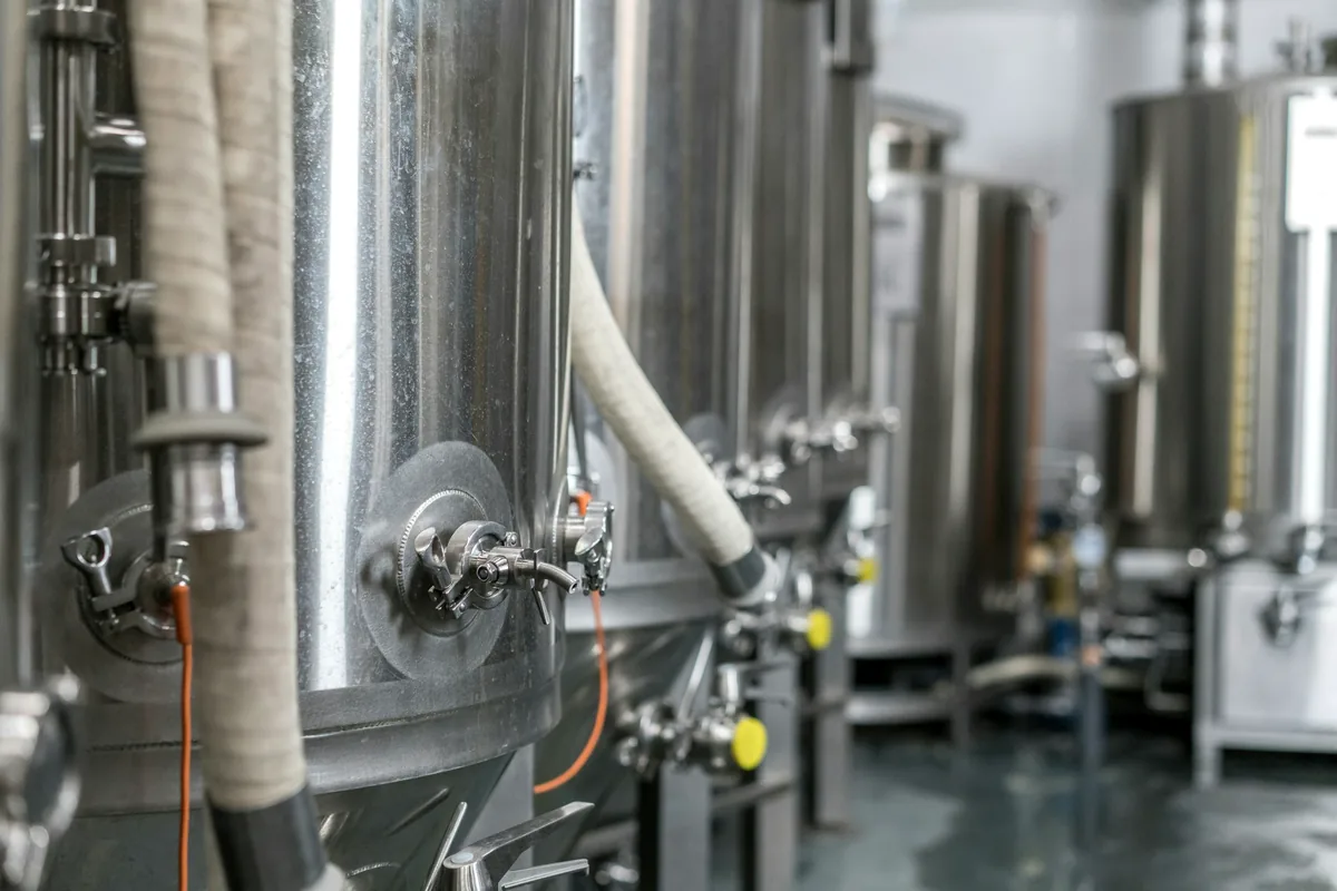 A row of stainless steel fermentation tanks and pipework in a brewery