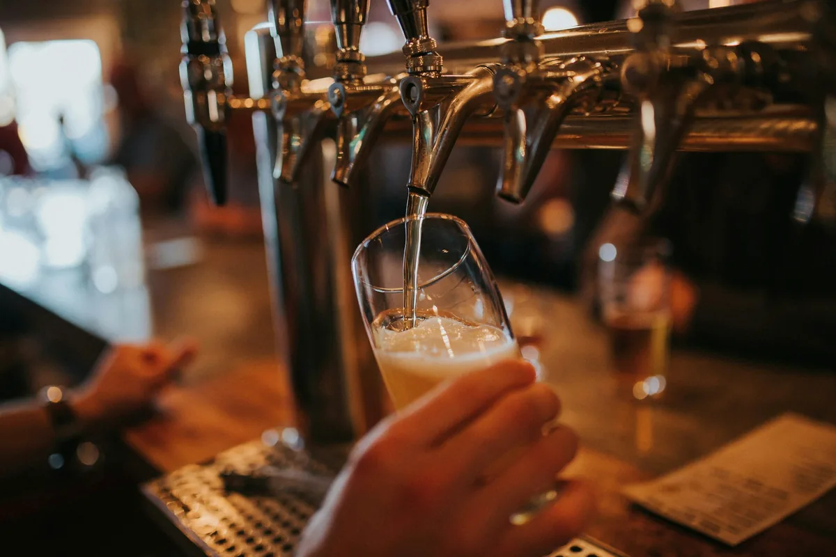 A glass held under a row of brass beer taps as it fills