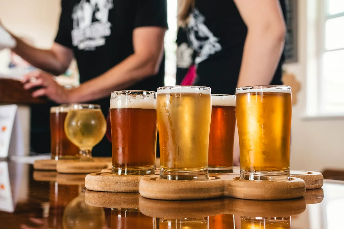 Several wooden flight paddles holding small glasses of beer and cider on a bar