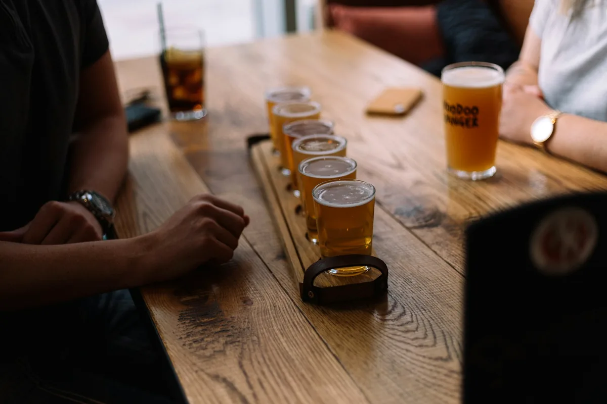 A row of small beer glasses on a table with two people sitting either side