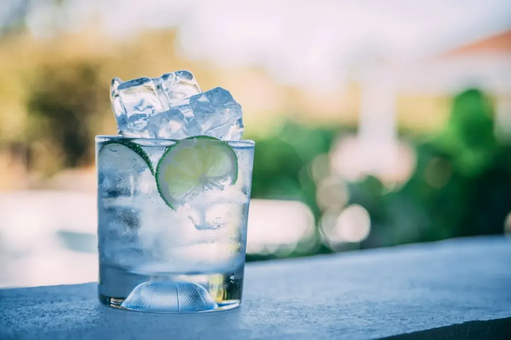 A tall glass of gin and tonic packed with ice and a slice of cucumber