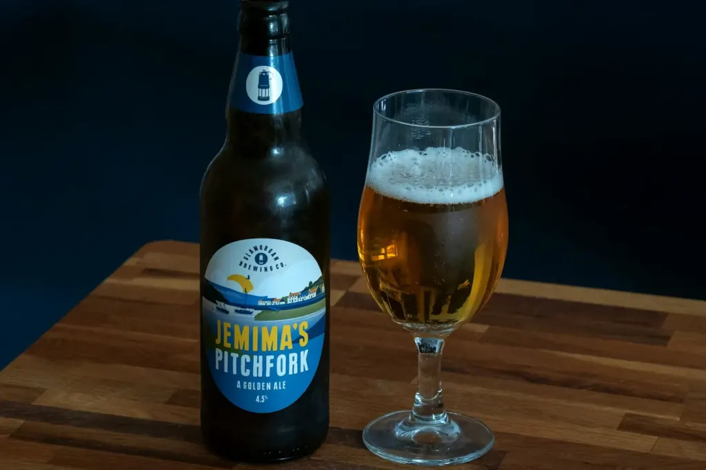 A pale golden ale with a white head in a stemmed tulip glass beside its bottle