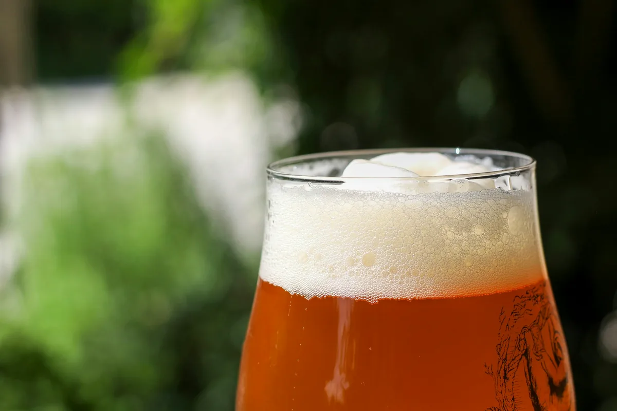 A glass of hazy amber ale with a white head, outdoors