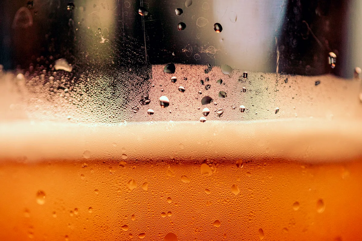 A cloudy wheat beer with a tall foam head in a condensation-covered glass