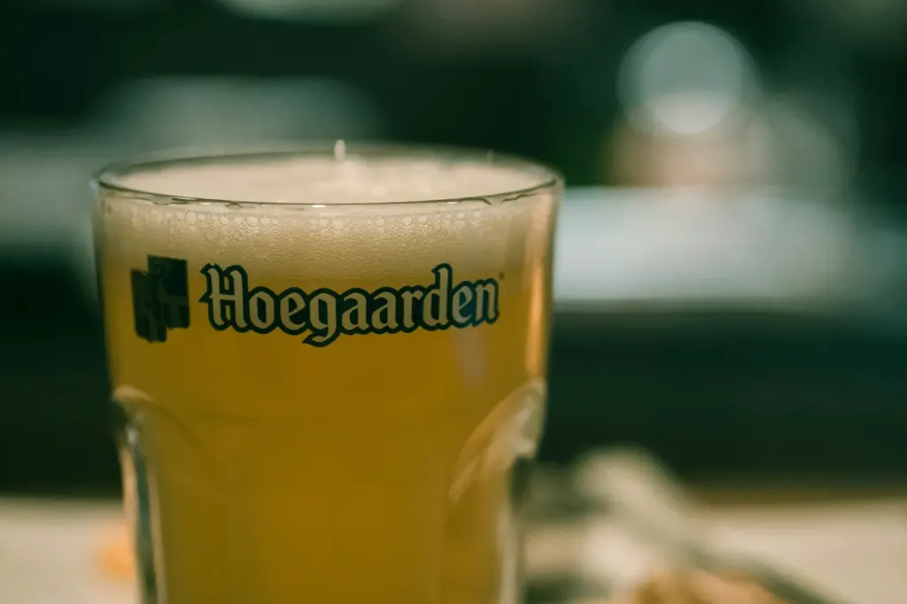 A cloudy pale wheat beer with a thick white head in a branded Hoegaarden glass