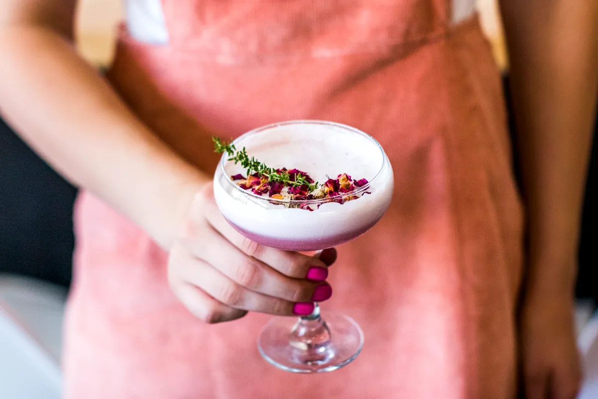 A hand holding a pink foam-topped cocktail in a stemmed coupe