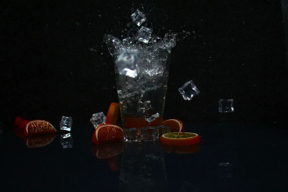 Ice cubes falling into a tall glass of clear liquid against a dark background
