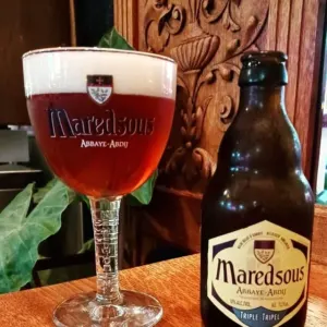 A Belgian abbey tripel poured into its branded chalice beside the bottle