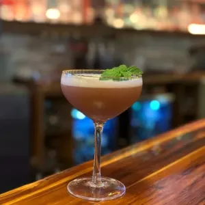 A coupe cocktail with a foam top and a mint garnish on the bar