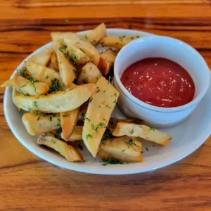 Hand cut frites topped with parsley, beside a dish of dipping sauce