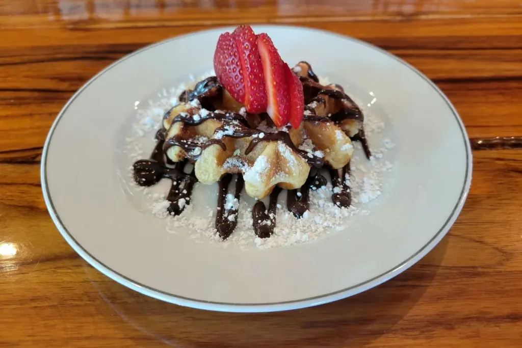 A Liege waffle with chocolate sauce, strawberries and powdered sugar on a white plate