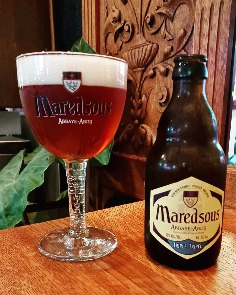 A Belgian abbey tripel poured into its branded chalice beside the bottle