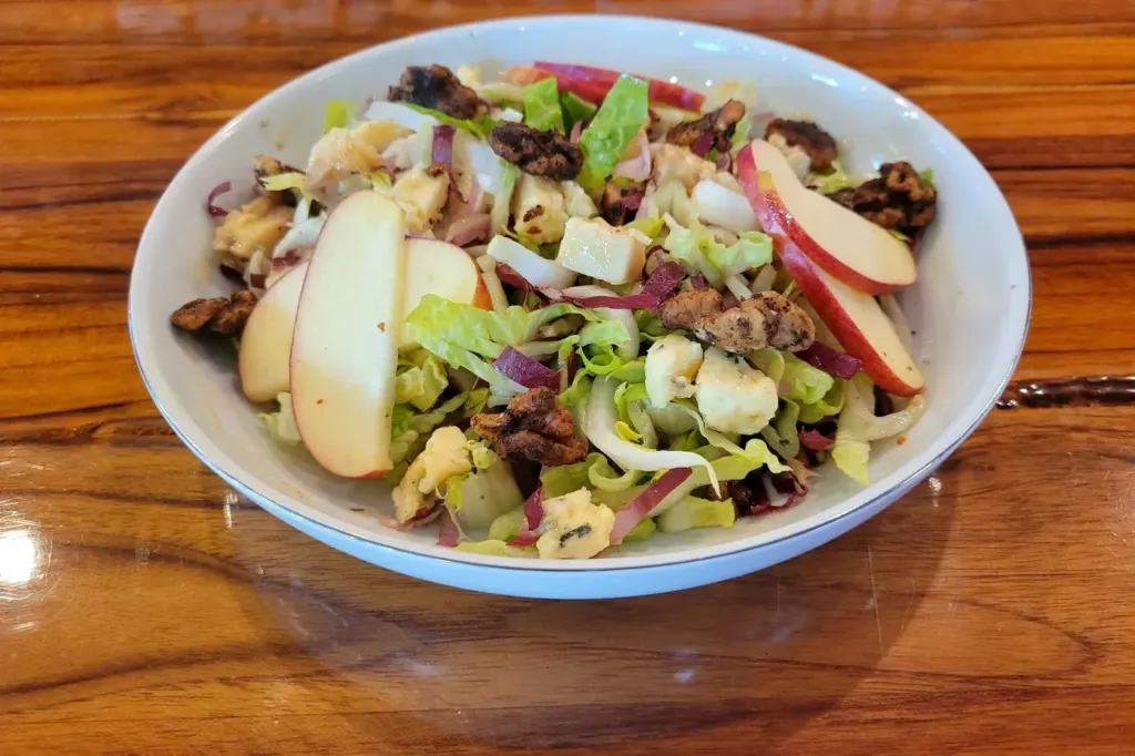 A white bowl of endive salad with apple slices, walnuts and blue cheese