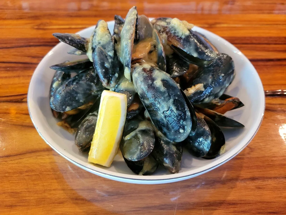 A white bowl of steamed mussels with a lemon wedge
