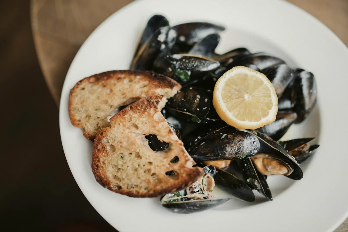 A plate of mussels with toasted bread and a lemon wedge