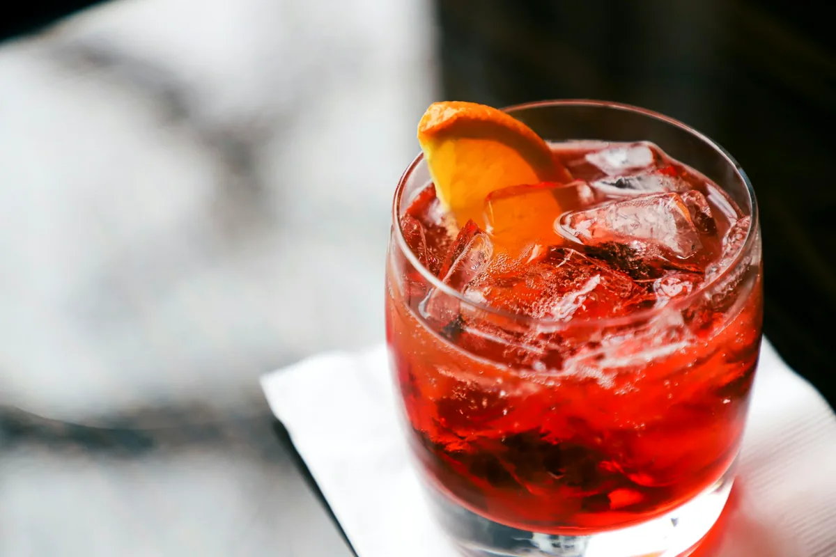 A red negroni cocktail over ice with an orange slice