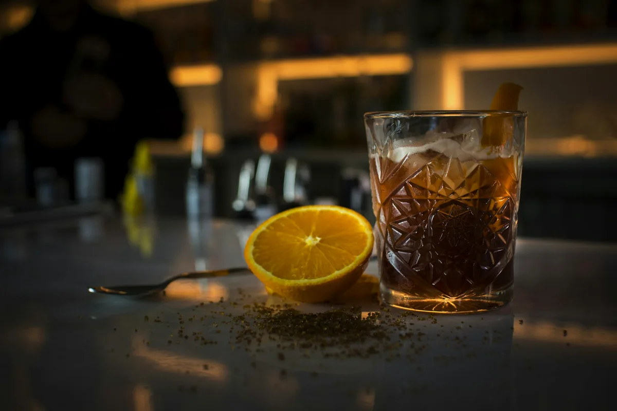 A tumbler of amber spirit beside a slice of orange on a bar counter