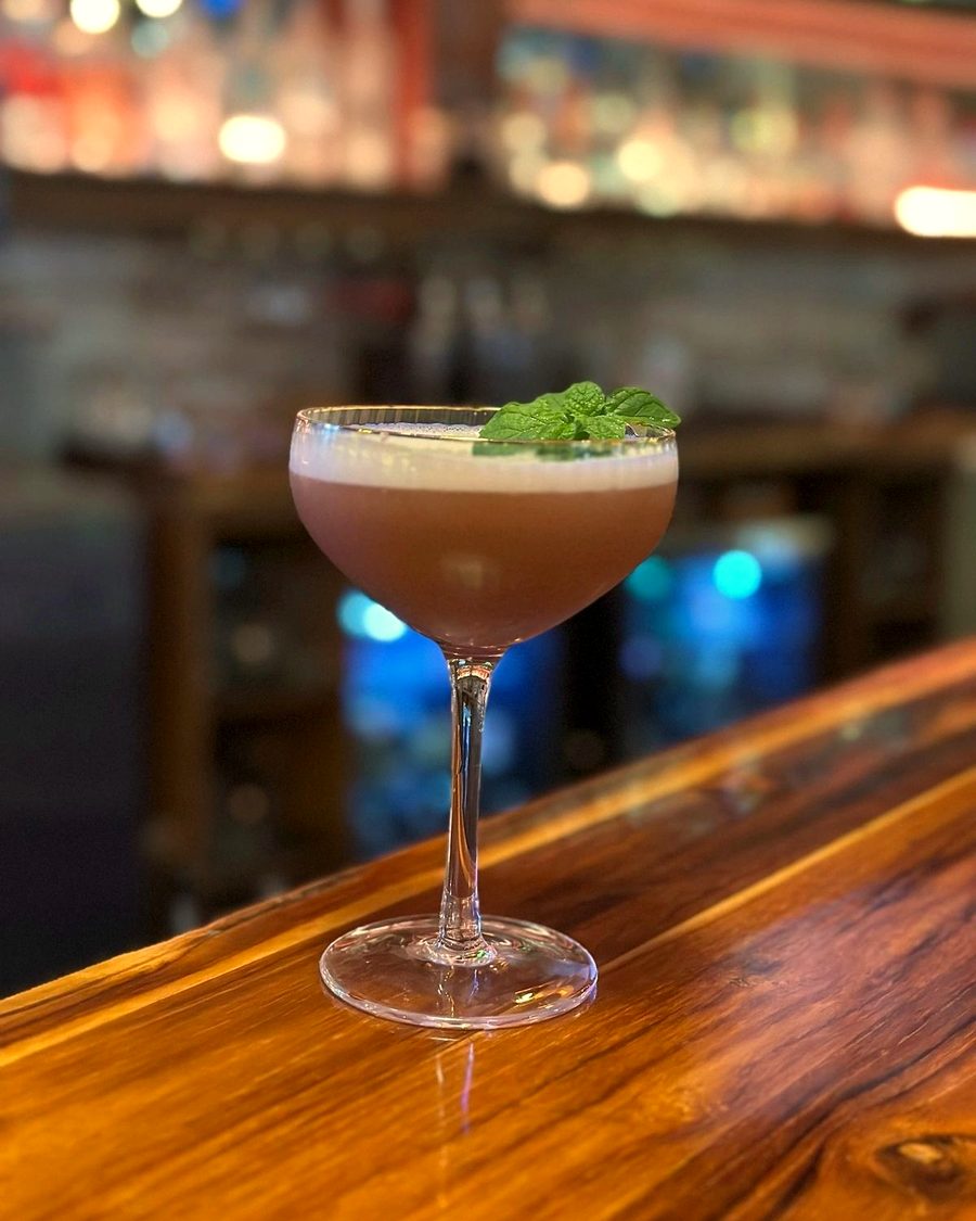 A clover club cocktail in a coupe with a mint garnish, on the bar at Meyboom Brasserie