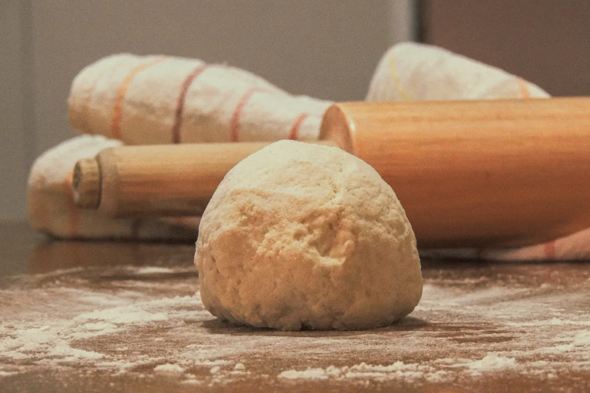 A ball of pastry dough on a floured table beside two rolling pins