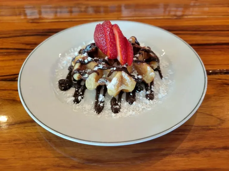 A Liege waffle under chocolate sauce, whipped cream and strawberries