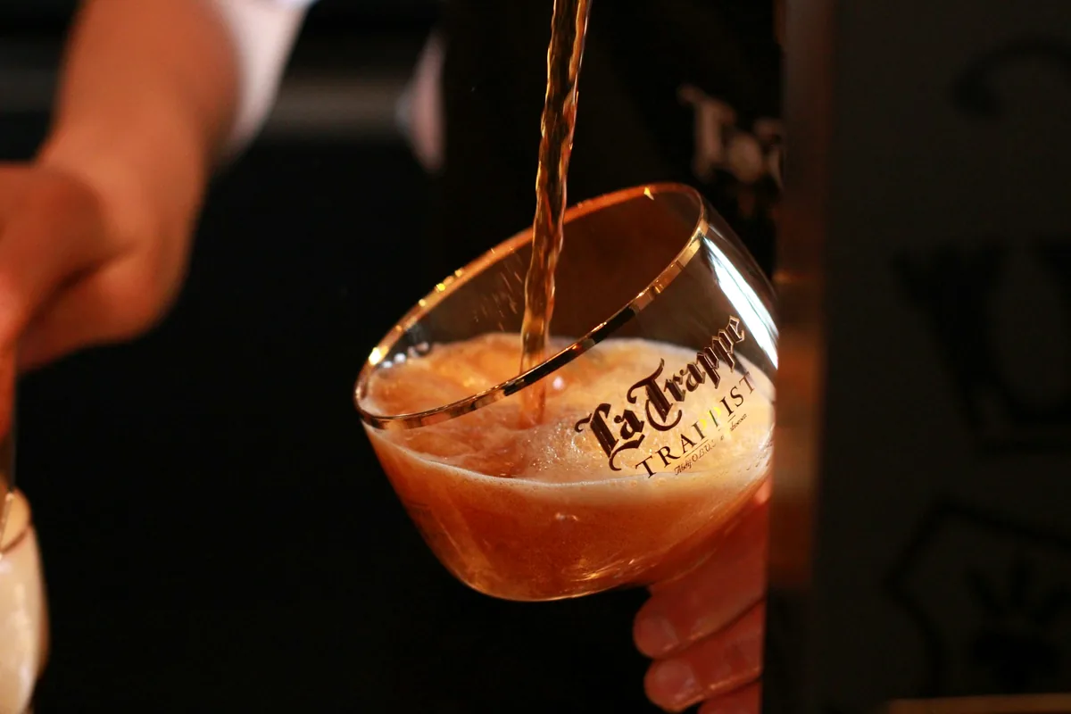 An amber Trappist ale being poured into a branded stemmed glass