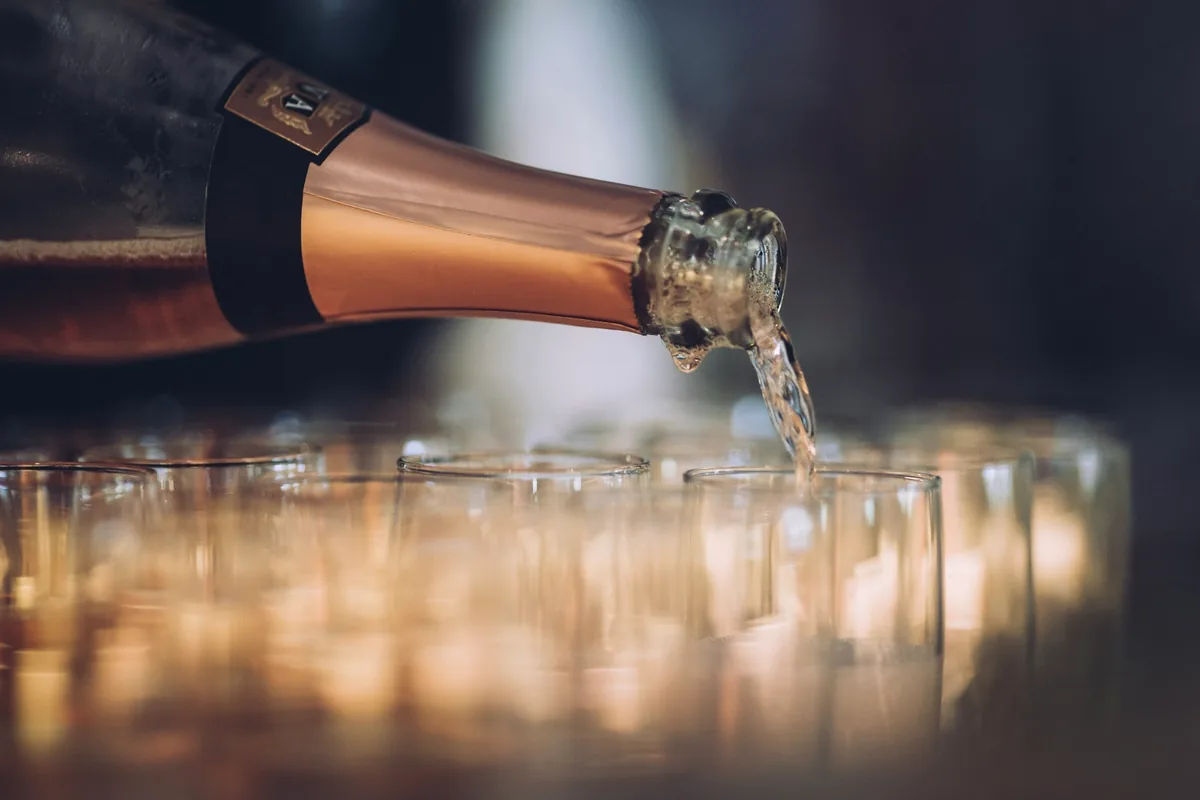 Sparkling wine poured from a bottle across a row of glasses