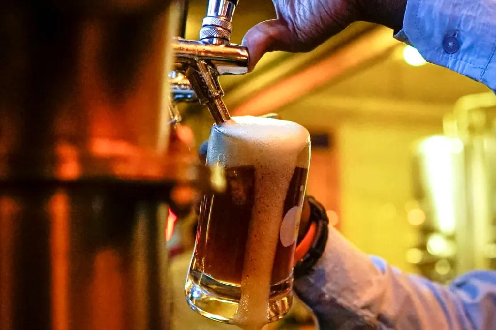 A glass of pale beer being filled from a tap handle behind a bar
