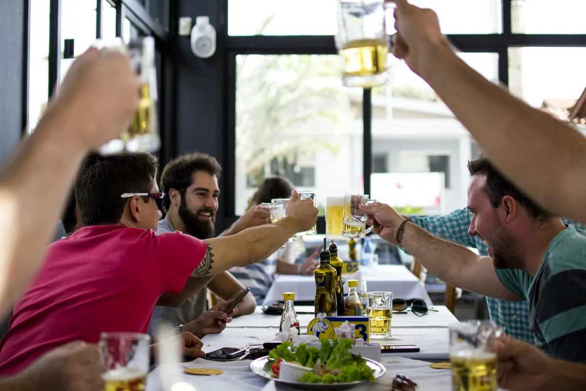 People at a table raising glasses of beer above a shared lunch