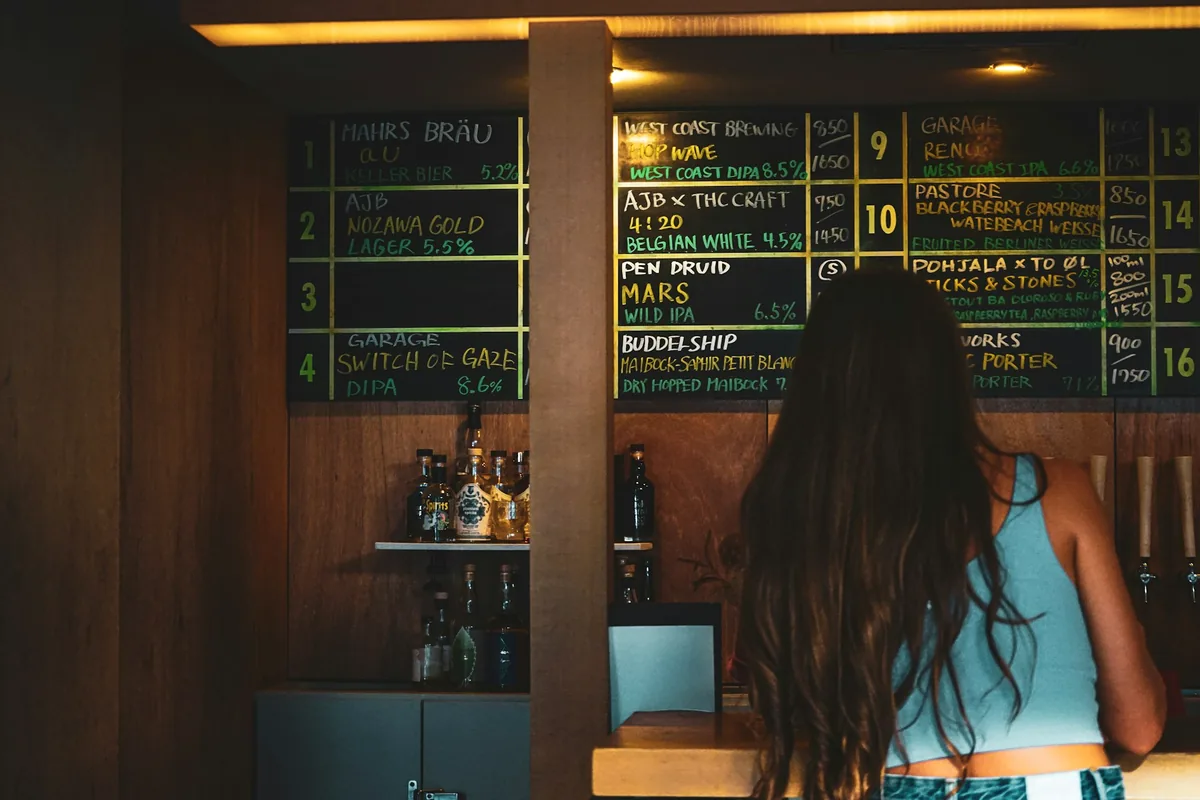 A person standing at a bar reading the menu board behind it