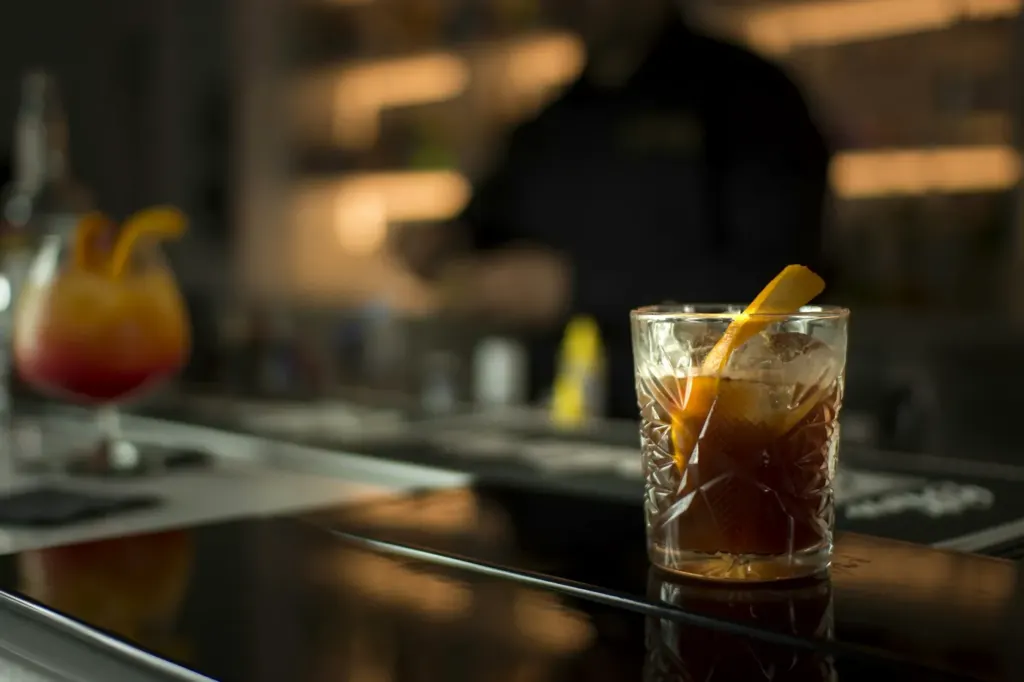 An amber cocktail in a rocks glass finished with a twist of orange peel