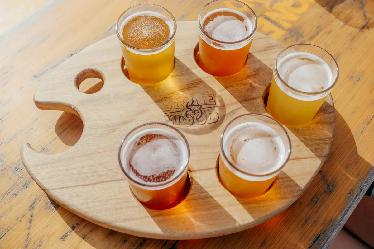 Four small tasting glasses of pale beer set into a round wooden paddle