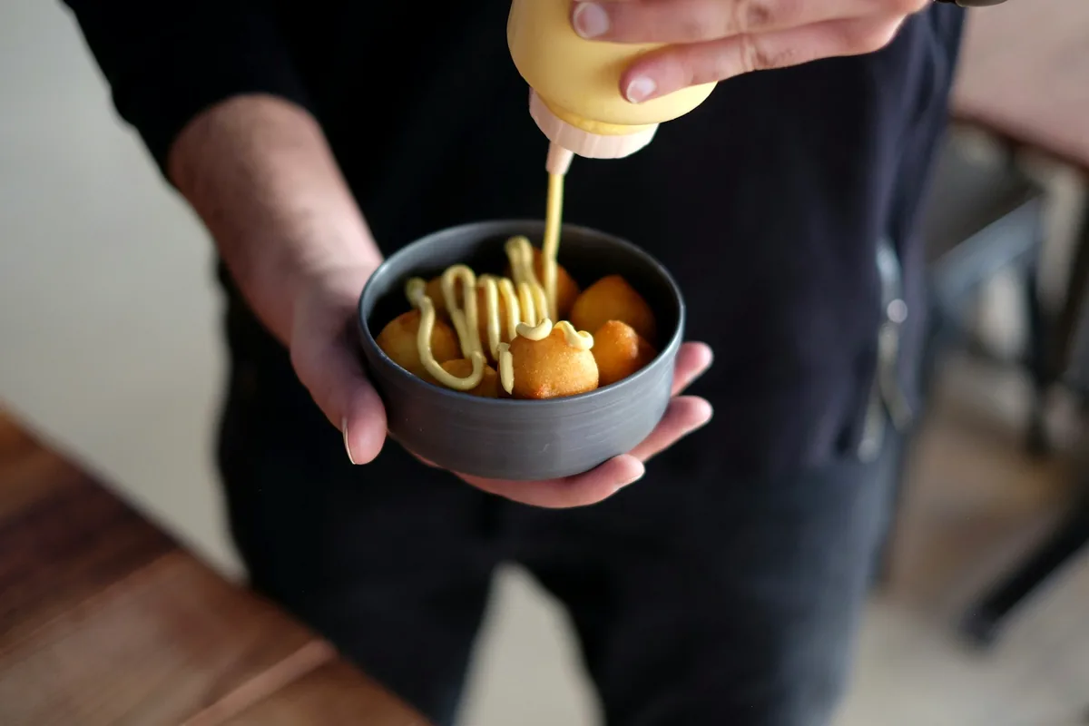 Sauce being squeezed from a bottle onto fried food in a bowl