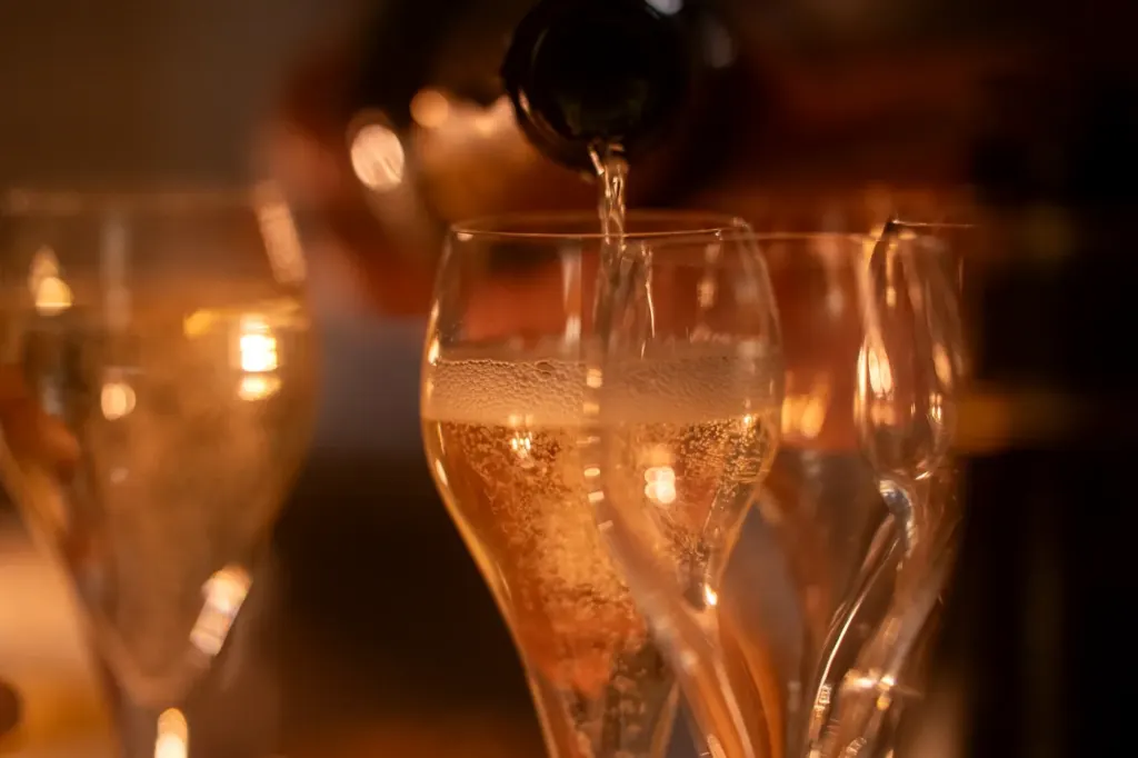 Sparkling wine poured into stemmed glasses under warm low light