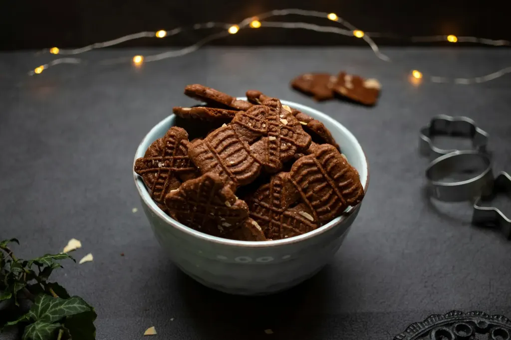 A bowl of stamped speculaas biscuits on a dark surface with string lights behind