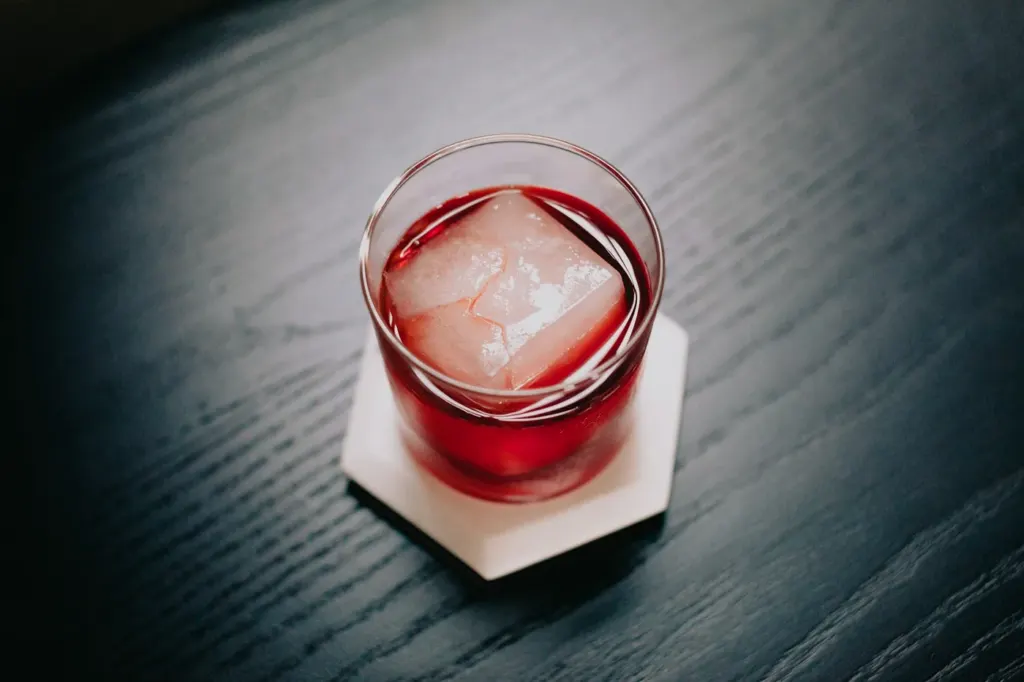 A deep red-amber cocktail over a single large ice cube in a rocks glass