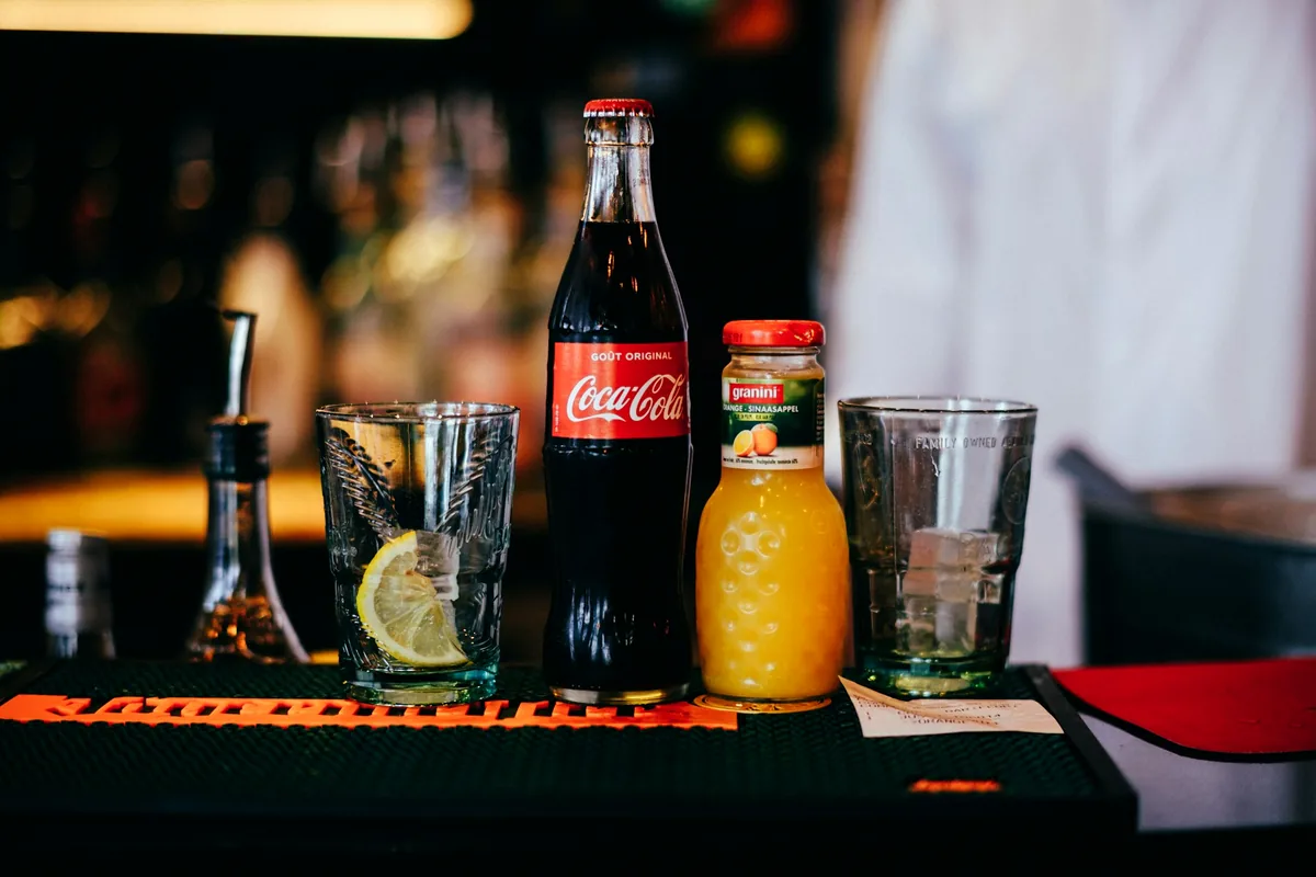 Spirit bottles, a cola bottle and empty glasses set out on a bar counter