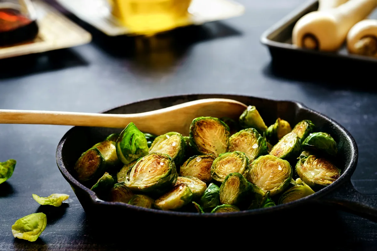 Halved Brussels sprouts browned in a cast iron pan with a wooden spoon