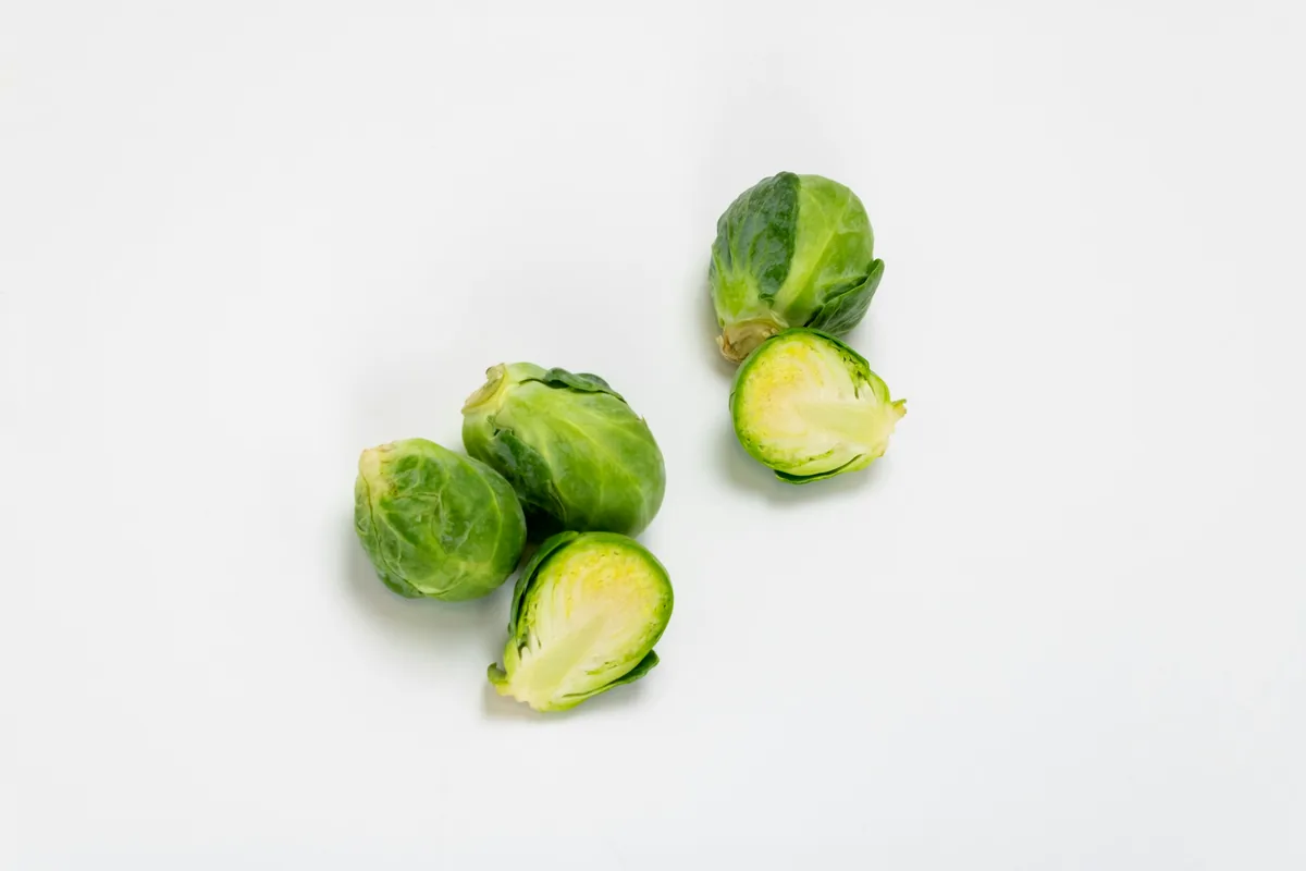Three Brussels sprouts, one halved, on a plain white surface