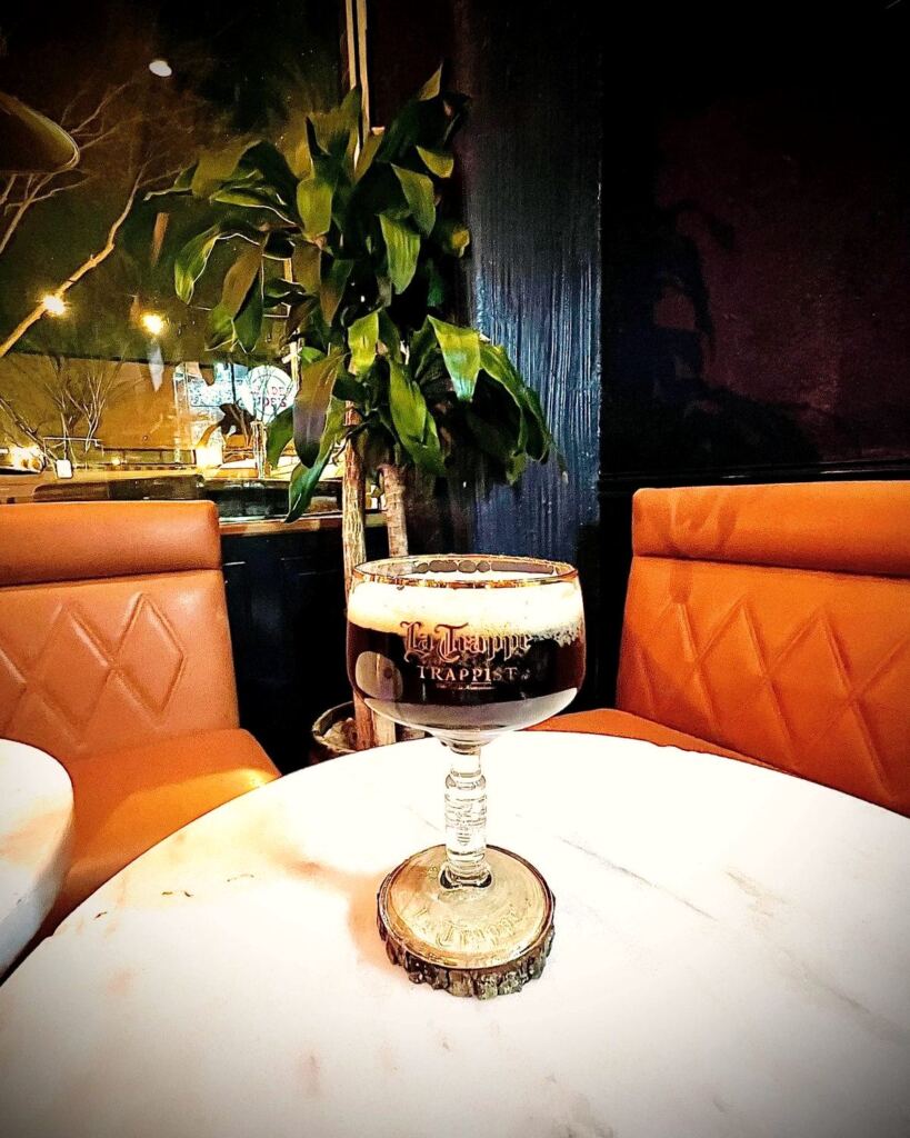 A La Trappe Trappist chalice on a marble table at Meyboom Brasserie, with tan leather banquettes and warm window light behind