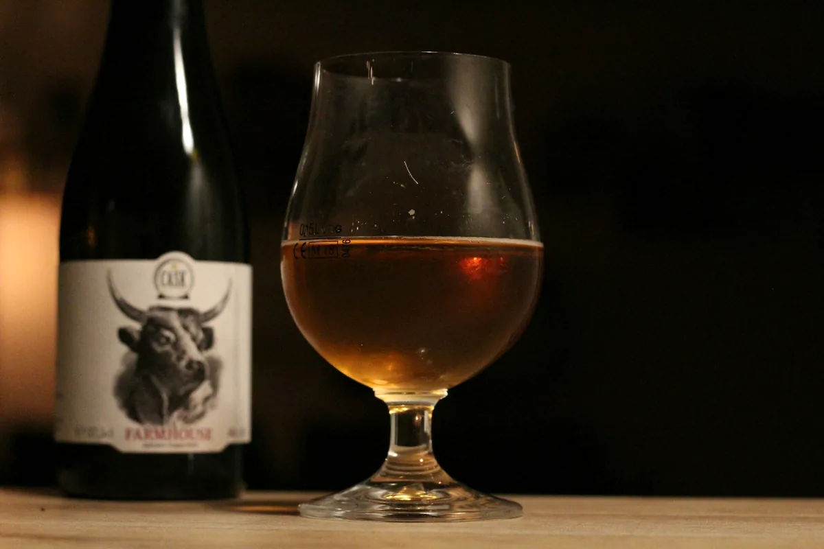 An amber-gold ale in a stemmed tulip glass on a dark table beside a bottle