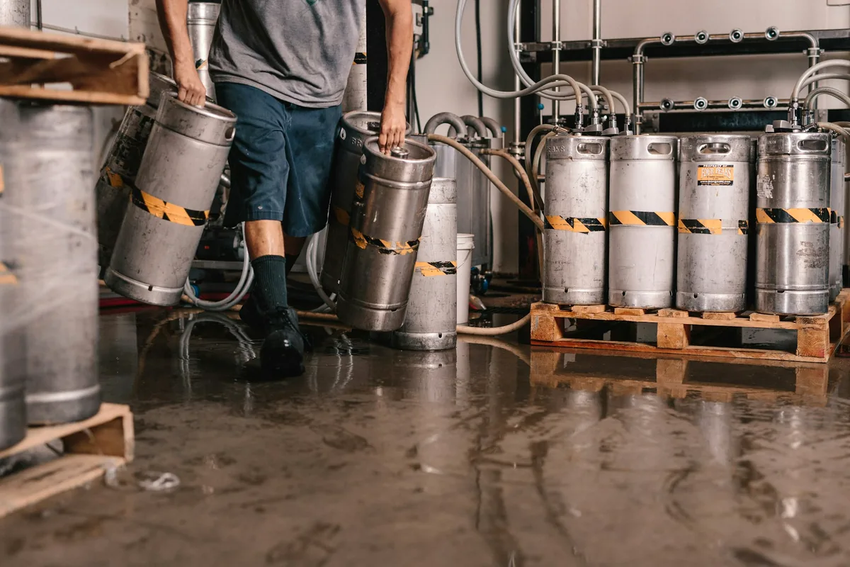 Steel tanks and stacked kegs on a wet brewery floor