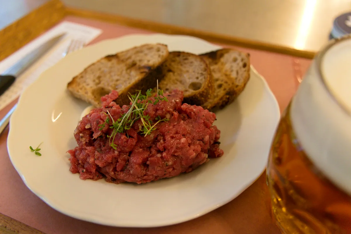 A plate of raw beef tartare with toasted bread and a glass of beer