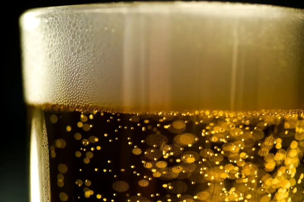 A pale lager in a glass with a thick white head and rising bubbles