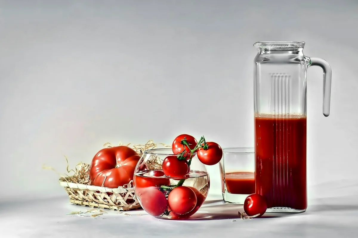 A glass jug of tomato juice beside a basket of tomatoes