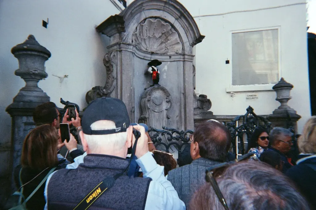 A crowd of visitors photographing the small Manneken Pis fountain statue in Brussels