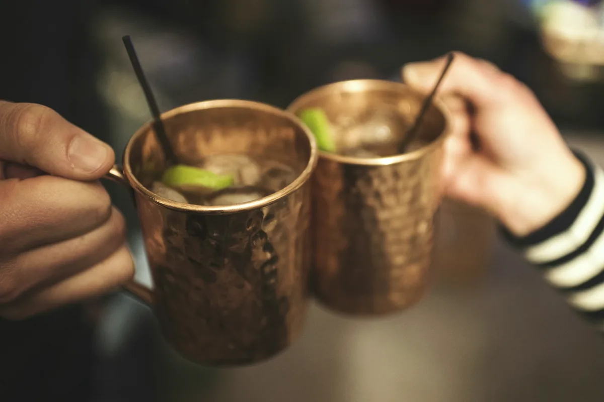 Two hands touching copper mule mugs together in a toast