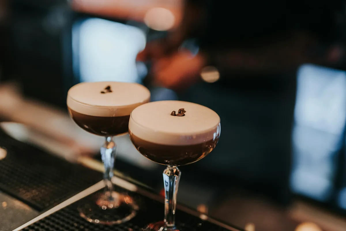 Two espresso martinis on a bar, each garnished with three coffee beans